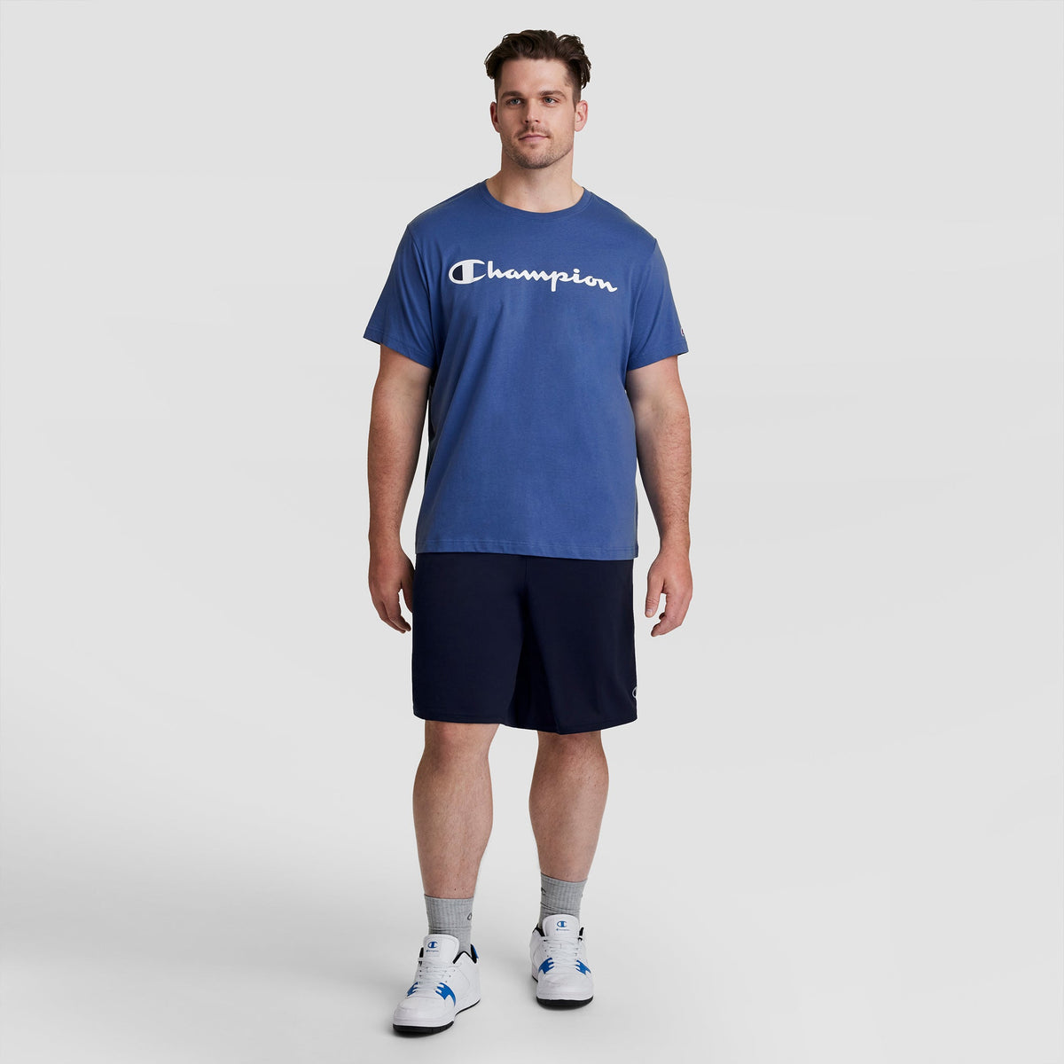 A man wearing a blue short-sleeved t-shirt and Champion 10″ Moisture Wicking, Sport Shorts - Big & Tall in dark blue.