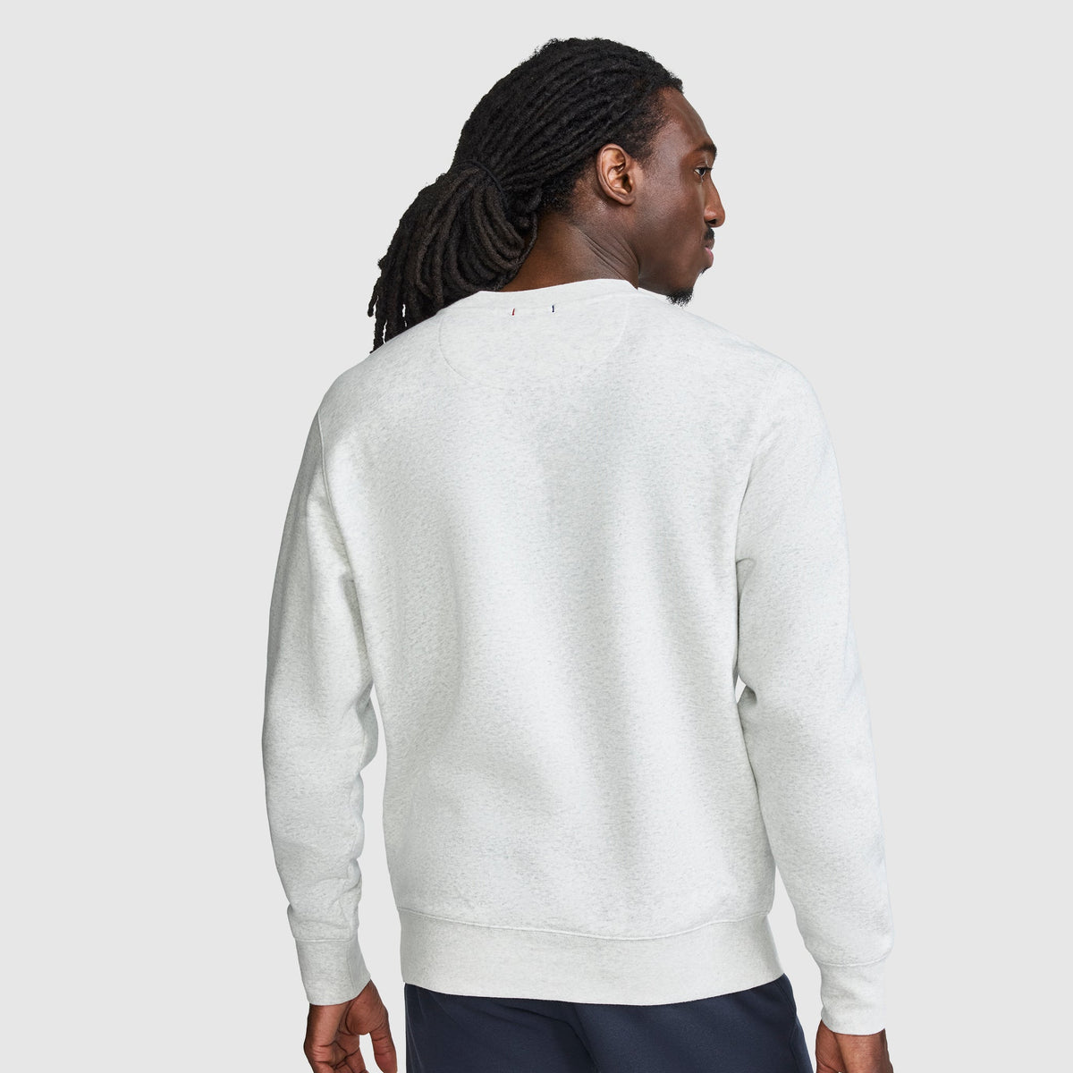 A person with long hair is shown from the back against a light gray background, wearing dark pants and the Champion Powerblend Crewneck Sweatshirt, Tonal Script Logo.