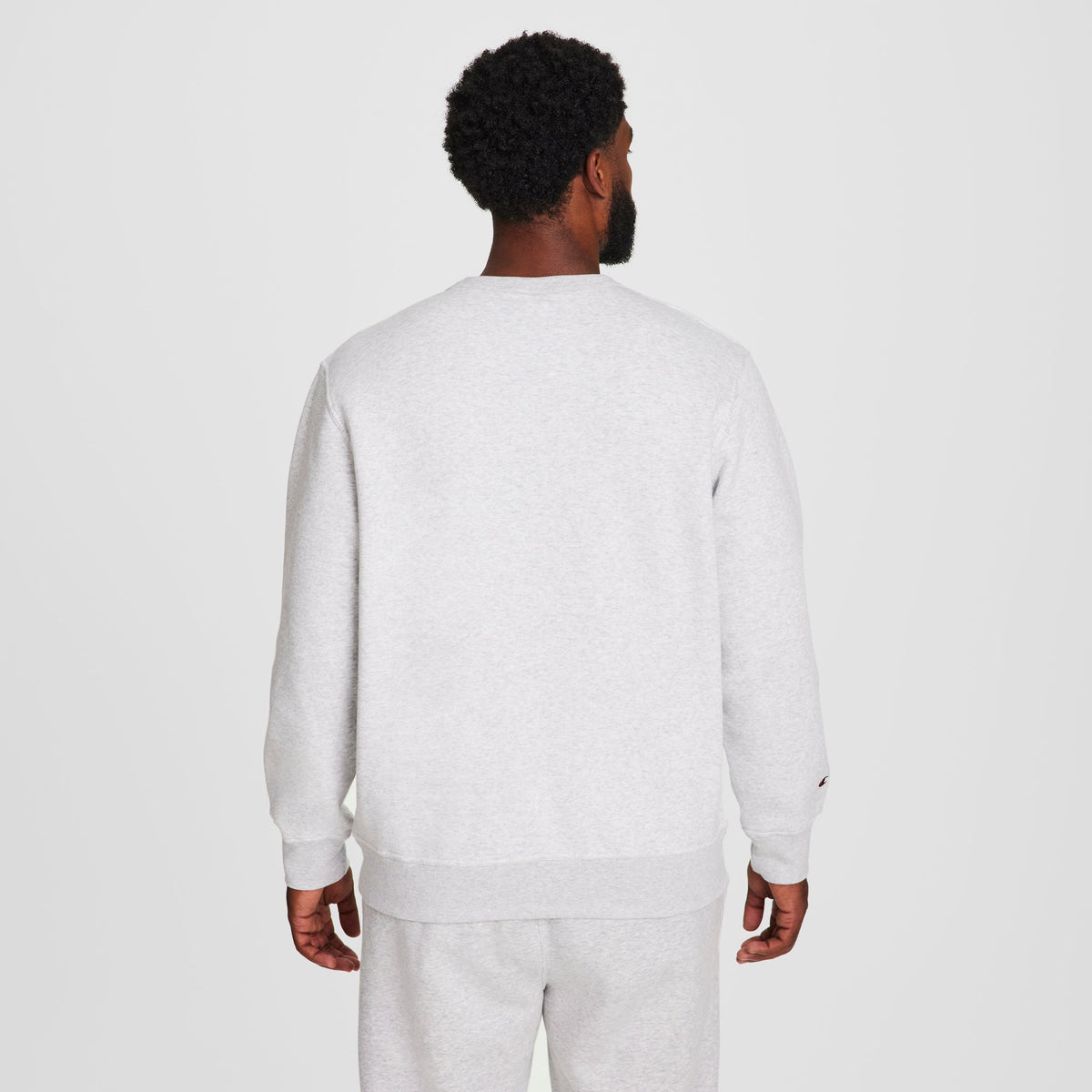 A man with short curly hair, seen from behind, wears a Champion Powerblend Crewneck Sweatshirt, C Logo - Big & Tall, along with matching sweatpants against a plain white background.