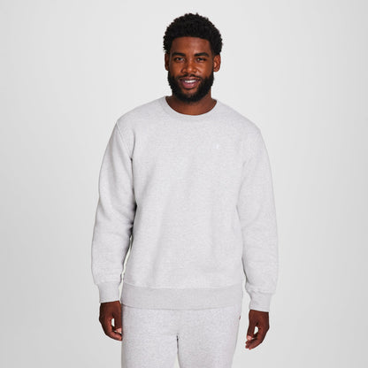 A man with short curly hair and a beard stands smiling in a Champion Powerblend Crewneck Sweatshirt, C Logo - Big & Tall, paired with matching sweatpants against a plain white background.
