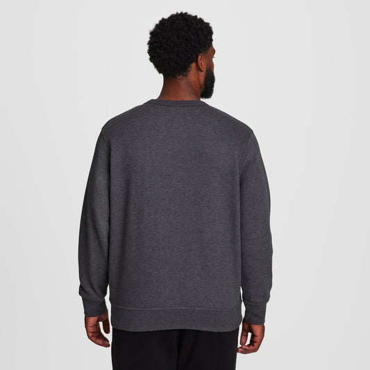A man with short curly hair faces away from the camera, wearing a dark gray Champion Powerblend Crewneck Sweatshirt, C Logo - Big & Tall, and black pants against a plain white background.