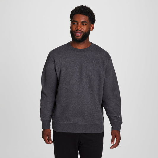 A man wearing Champion's Powerblend Crewneck Sweatshirt, C Logo - Big & Tall in dark gray and black pants smiles against a light gray background.