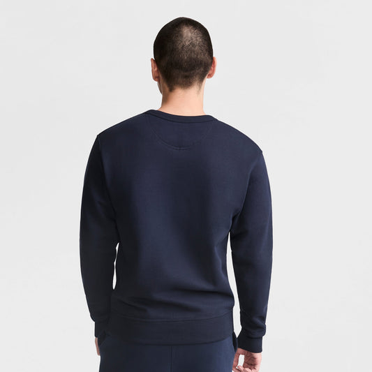 A person with short hair faces away, wearing a dark navy Champion Powerblend Crewneck Sweatshirt with C Logo and matching pants, against a plain white background.