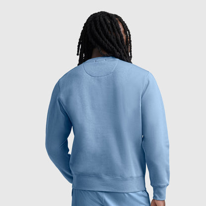 A person with long dreadlocks is shown from behind, wearing a light blue Champion Powerblend Crewneck Sweatshirt with the C logo and matching athletic fleece pants against a plain light gray background.
