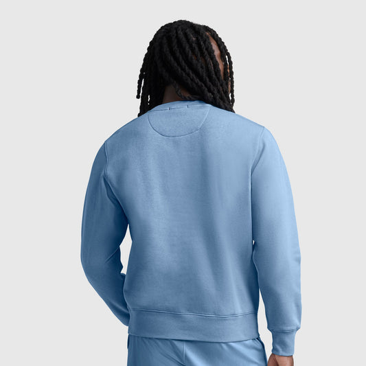 A person with long dreadlocks is shown from behind, wearing a light blue Champion Powerblend Crewneck Sweatshirt with the C logo and matching athletic fleece pants against a plain light gray background.