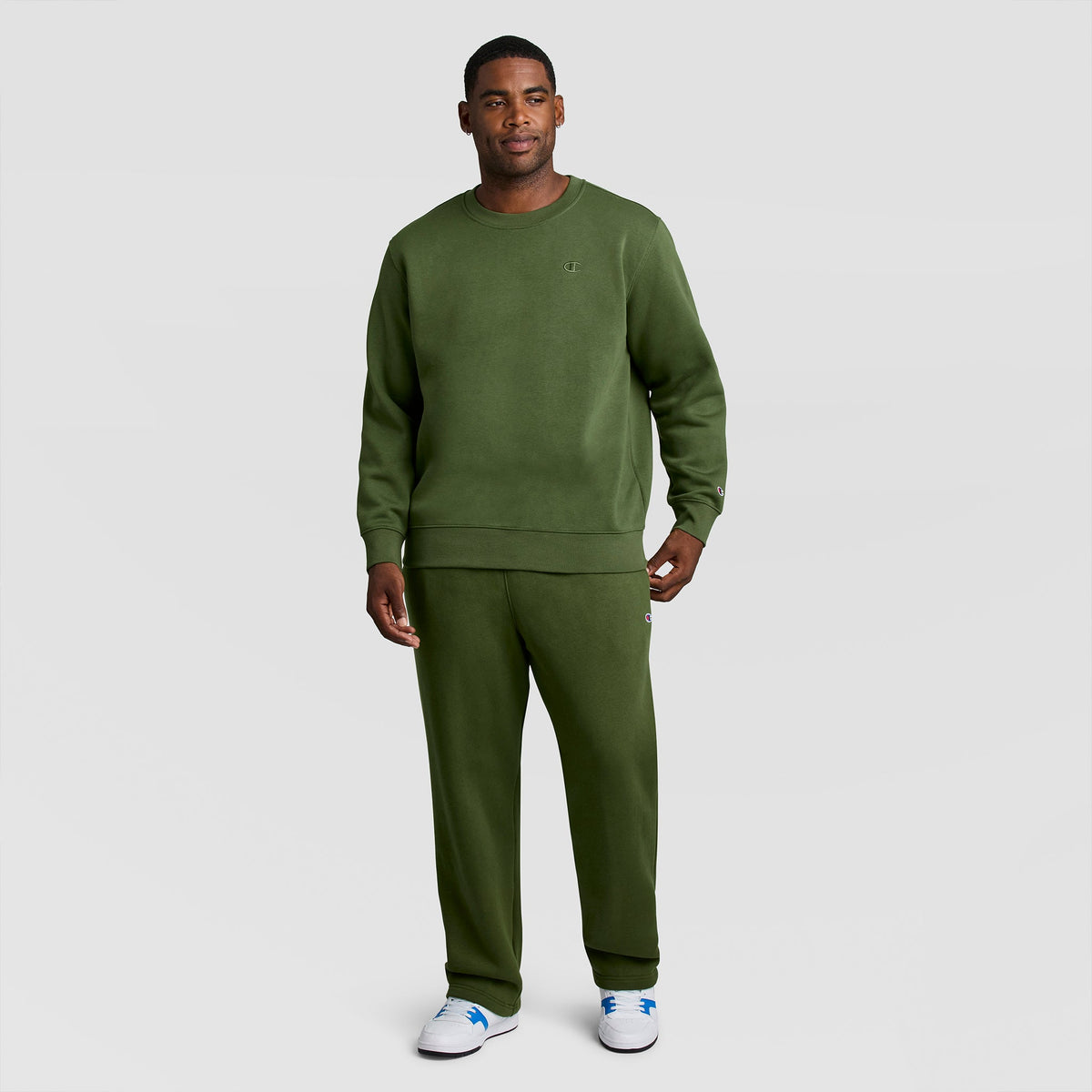 A man wearing an olive green Champion Powerblend Crewneck Sweatshirt, C Logo - Big & Tall and matching sweatpants.