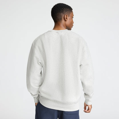 A person with short hair, seen from behind, wears a light gray Champion Reverse Weave Crewneck Sweatshirt, C Logo, and dark pants against a plain white background.