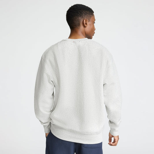 A person with short hair, seen from behind, wears a light gray Champion Reverse Weave Crewneck Sweatshirt, C Logo, and dark pants against a plain white background.