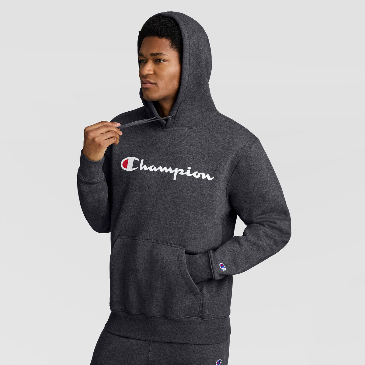 A charcoal gray Champion Powerblend Hoodie, Full Script Logo, with a white script logo across the chest and a small logo patch on the left sleeve.
