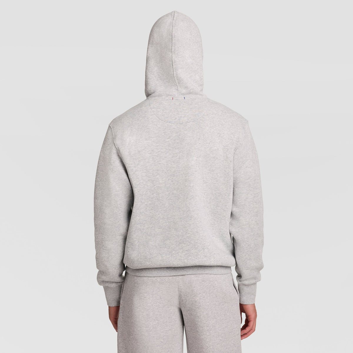 A person is shown from the back with the hood up, wearing the Champion Powerblend Hoodie, Full Script Logo in light gray along with matching sweatpants, standing against a plain white background.
