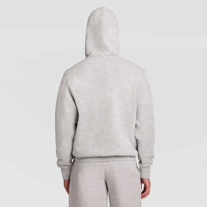 A person is shown from the back with the hood up, wearing the Champion Powerblend Hoodie, Full Script Logo in light gray along with matching sweatpants, standing against a plain white background.