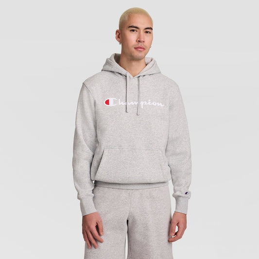A person with short blond hair wears a light gray Champion Powerblend Hoodie with a full script logo and matching sweatpants, standing against a plain light gray background.
