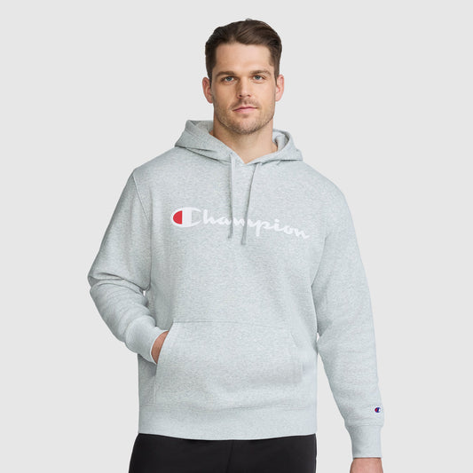 A man wears a heather gray midweight Champion Powerblend Hoodie, Full Script Logo - Big & Tall, with a large logo across the chest and a hand in the front kangaroo pocket.