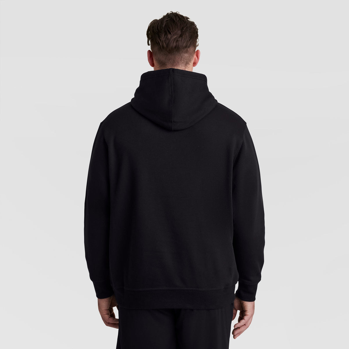 A person seen from behind wearing a black Champion Powerblend Hoodie, Full Script Logo - Big & Tall.