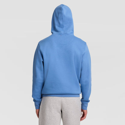A person wearing the Champion Powerblend Hoodie, Full Script Logo in blue and light gray sweatpants stands facing away from the camera against a plain light background.