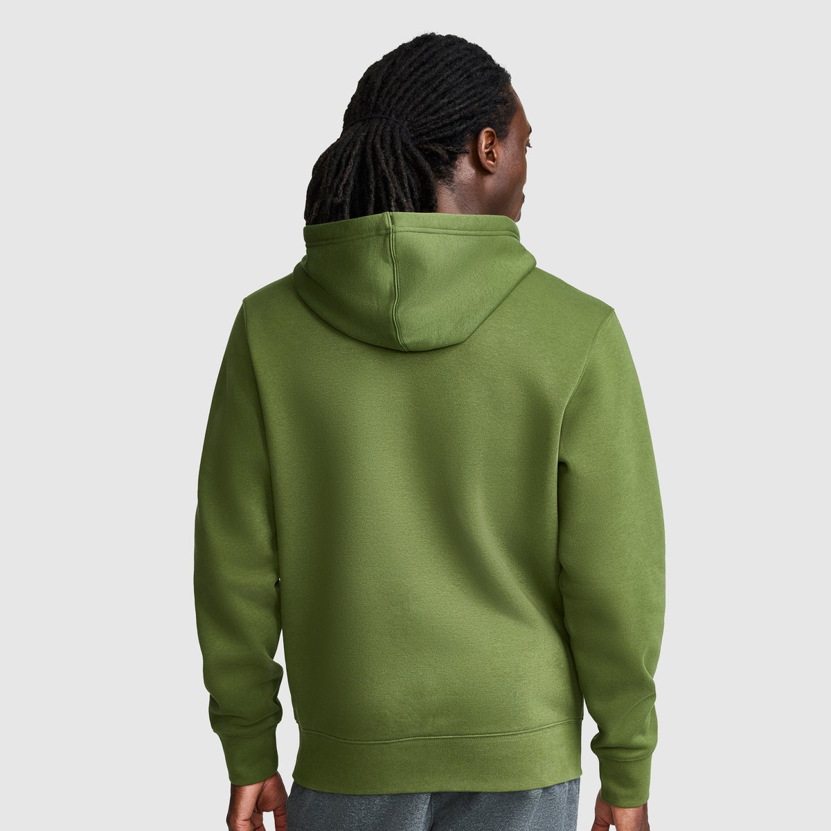A person with long, dark hair is shown from the back, wearing a Champion Powerblend Hoodie with Full Script Logo in green and gray pants, standing against a plain light gray background.