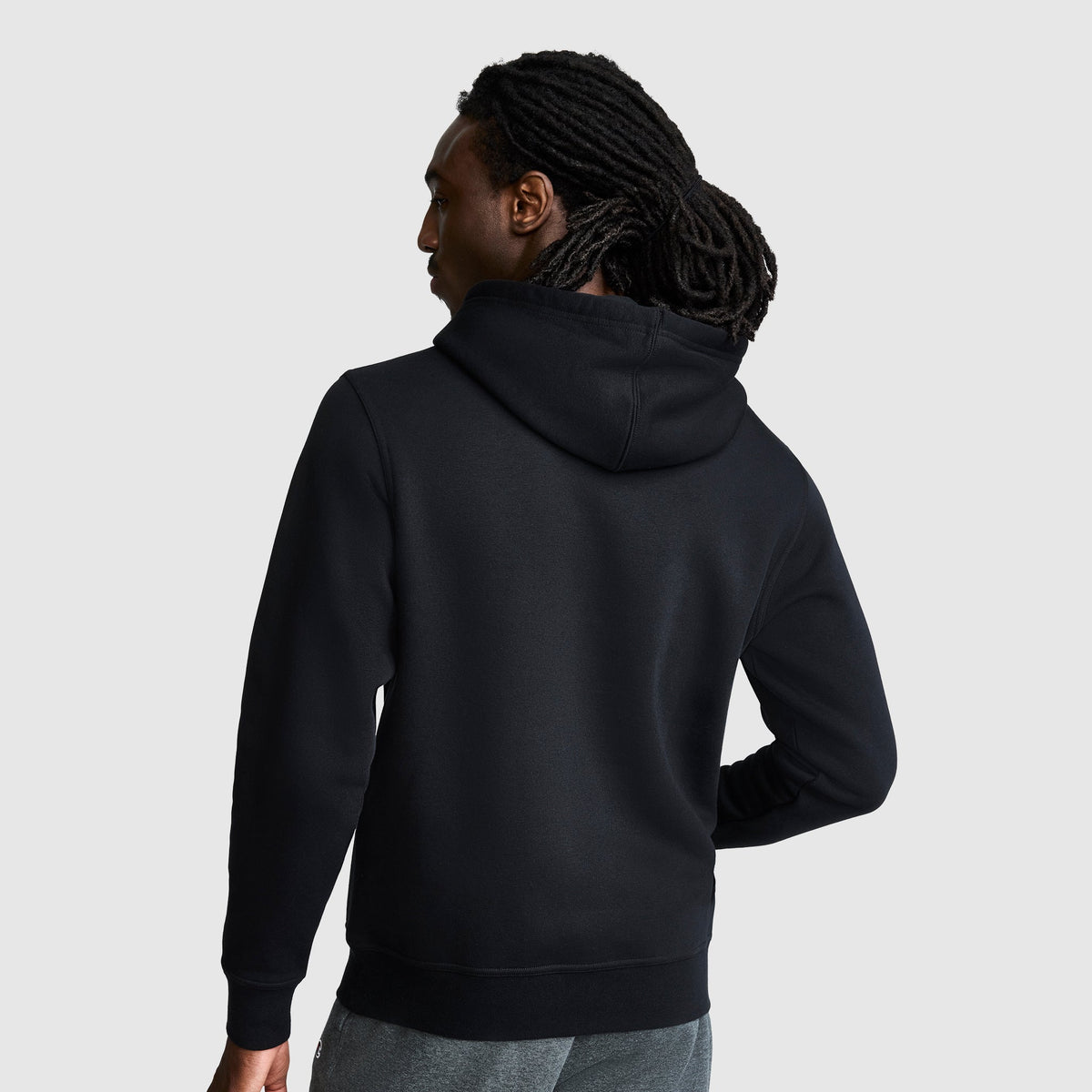 A person with long, dark dreadlocks stands facing away, wearing a black Champion Powerblend Hoodie with a tonal script logo and gray pants against a plain light gray background.
