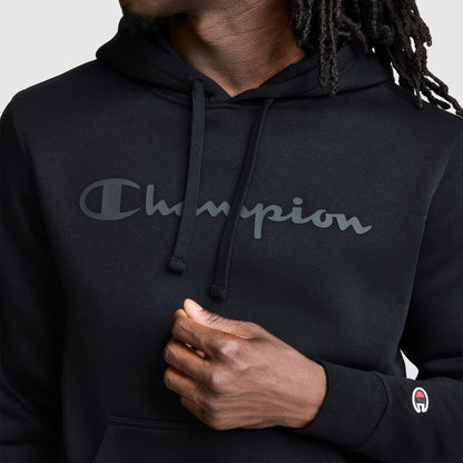 A person wearing a black Champion Powerblend Hoodie, Tonal Script Logo with a classic script logo across the chest and a small logo patch on the sleeve.