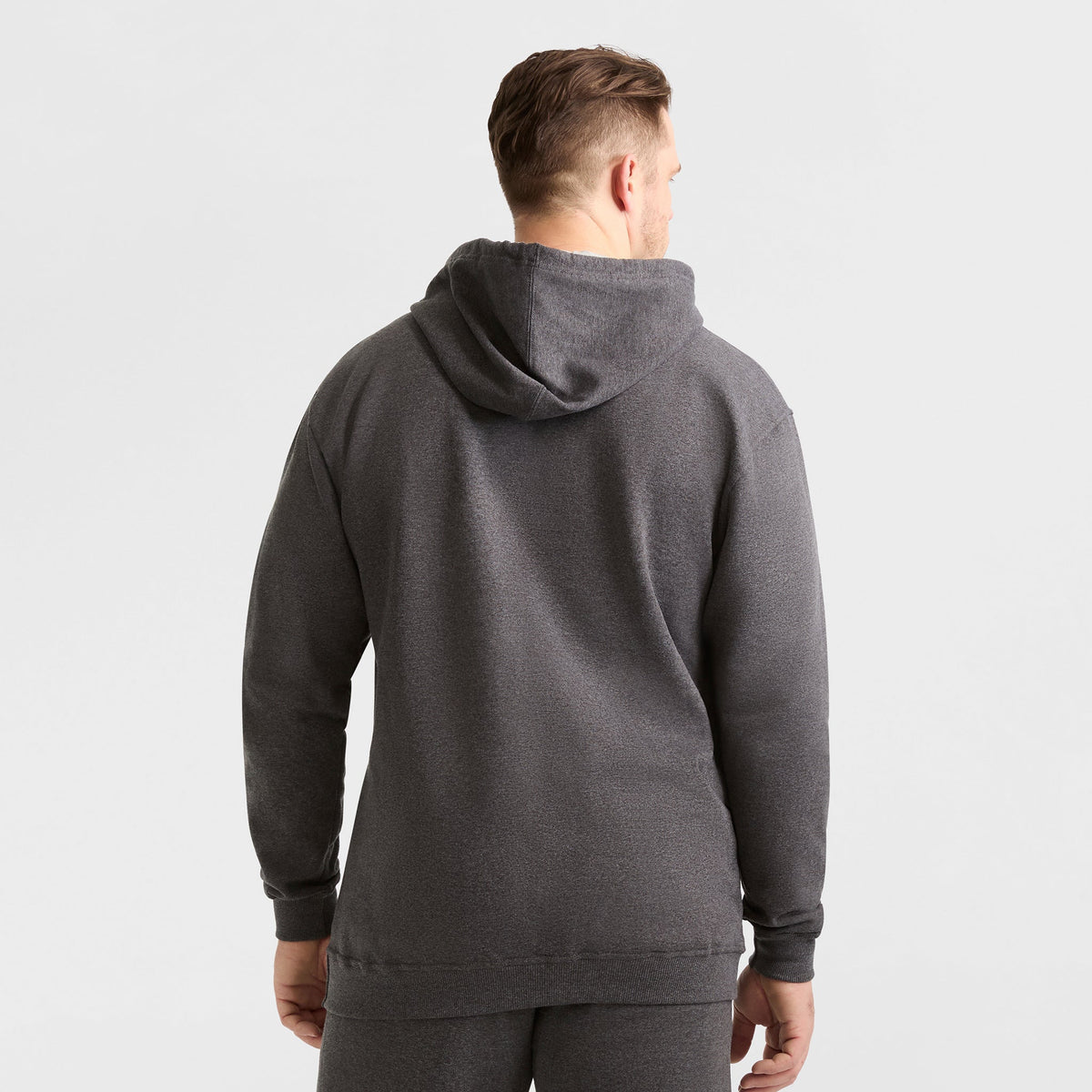 A man faces away from the camera, wearing a Champion Powerblend Hoodie, C Logo - Big & Tall in dark grey with matching pants, set against a plain light background.
