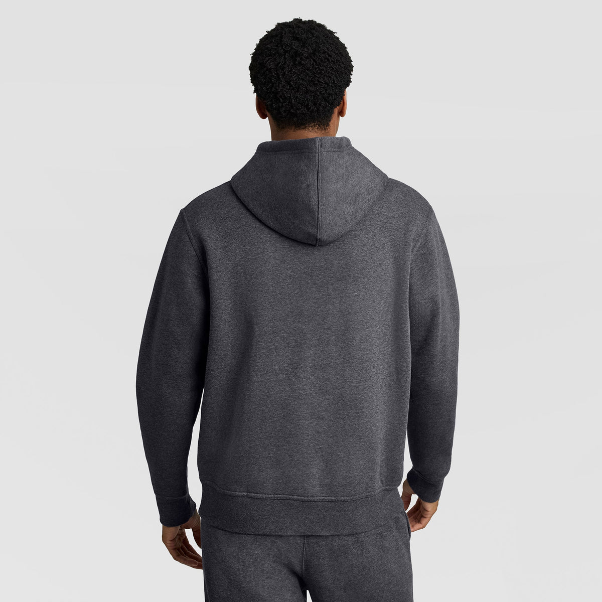 A person wearing the Champion Powerblend Hoodie, C Logo in dark gray, with matching sweatpants, is standing with their back to the camera against a plain light gray background.