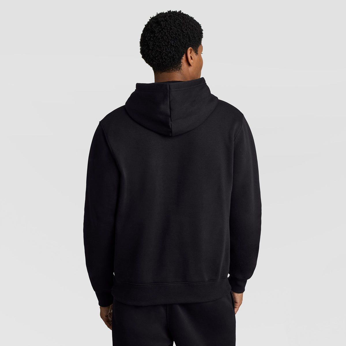 A person wearing a black Champion Powerblend Hoodie, C Logo, and black pants is standing with their back to the camera against a plain light background.