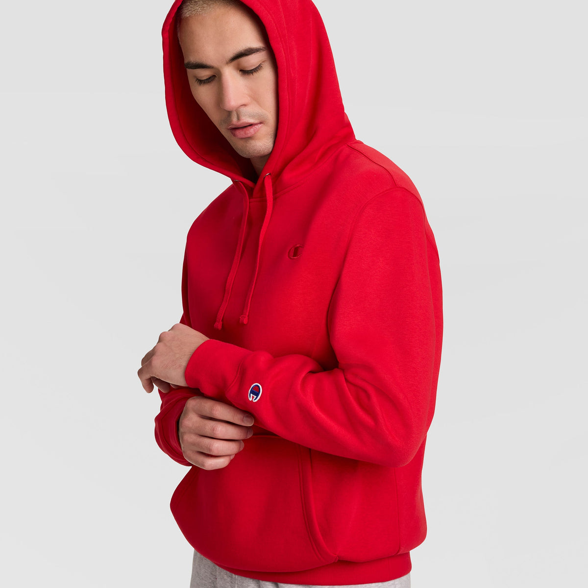 A person wearing a red Champion Powerblend Hoodie, C Logo, with a logo on the chest and a patch on the sleeve.