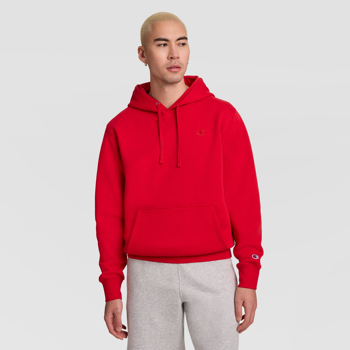 A person wearing a red Champion Powerblend Hoodie, C Logo, with a front pocket and a small logo on the chest and left sleeve.