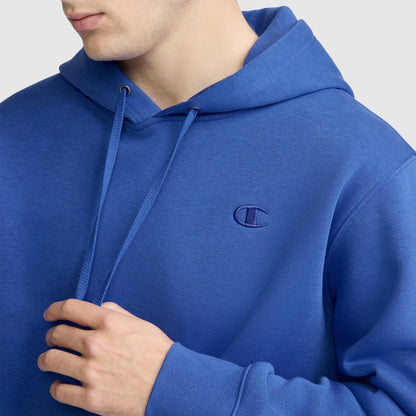 A person wearing a royal blue Champion Powerblend Hoodie, C Logo, featuring the Champion logo on the chest, adjusts the drawstring. The background is light gray.
