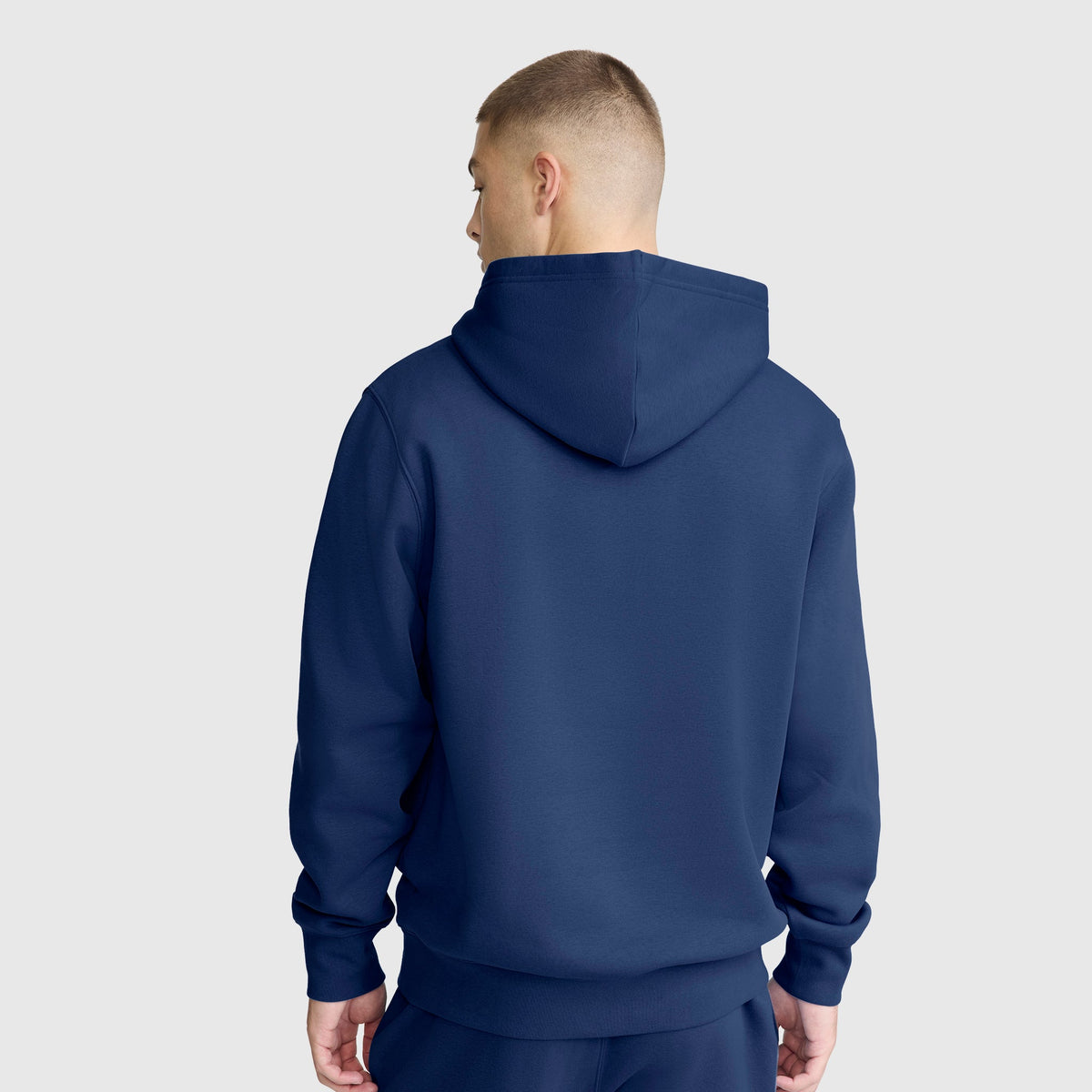 A person wears a Champion Powerblend Hoodie, C Logo in navy blue with matching pants, standing with their back to the camera against a plain light background.