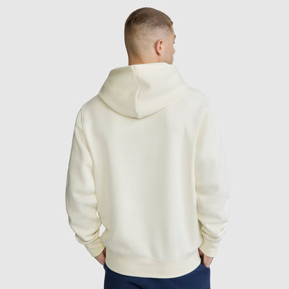 A man with short hair, seen from behind, is wearing the Champion Powerblend Hoodie, C Logo in off-white with dark pants against a plain light gray background.