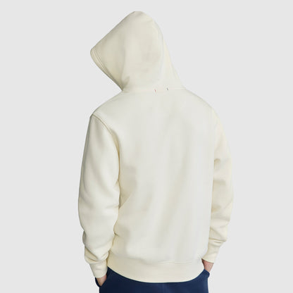 A person is wearing a Champion Powerblend Hoodie, C Logo, in off-white with the hood up, facing away from the camera. The men’s hooded sweatshirt appears plain, and the individual has their hands in their pockets. The background is light gray.