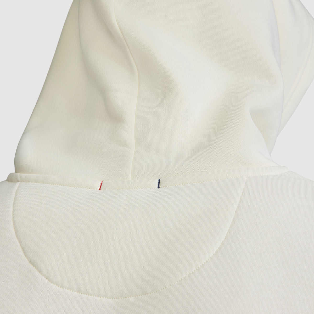 Close-up of the back of the cream-colored Champion Powerblend Hoodie, C Logo, highlighting the visible hood seam and small red and blue stitches near the neckline that showcase the classic fleece hoodie details.