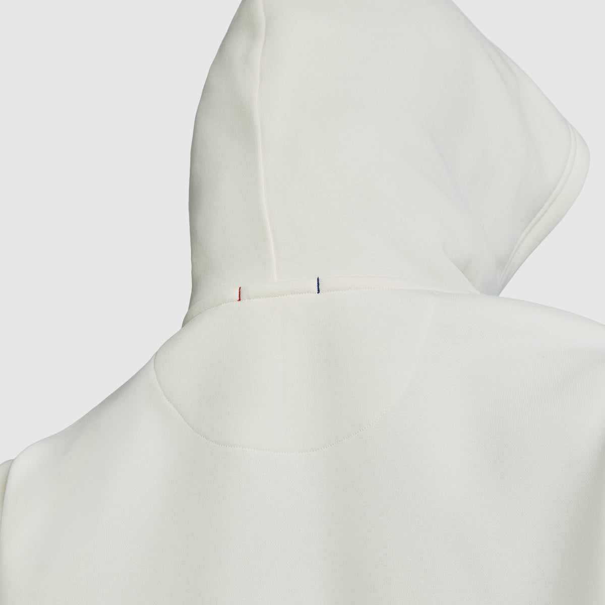 Close-up of the back of the Champion Powerblend Hoodie, C Logo, in white fleece, highlighting its minimal stitching detail and two small vertical stitches in red and blue near the top seam.