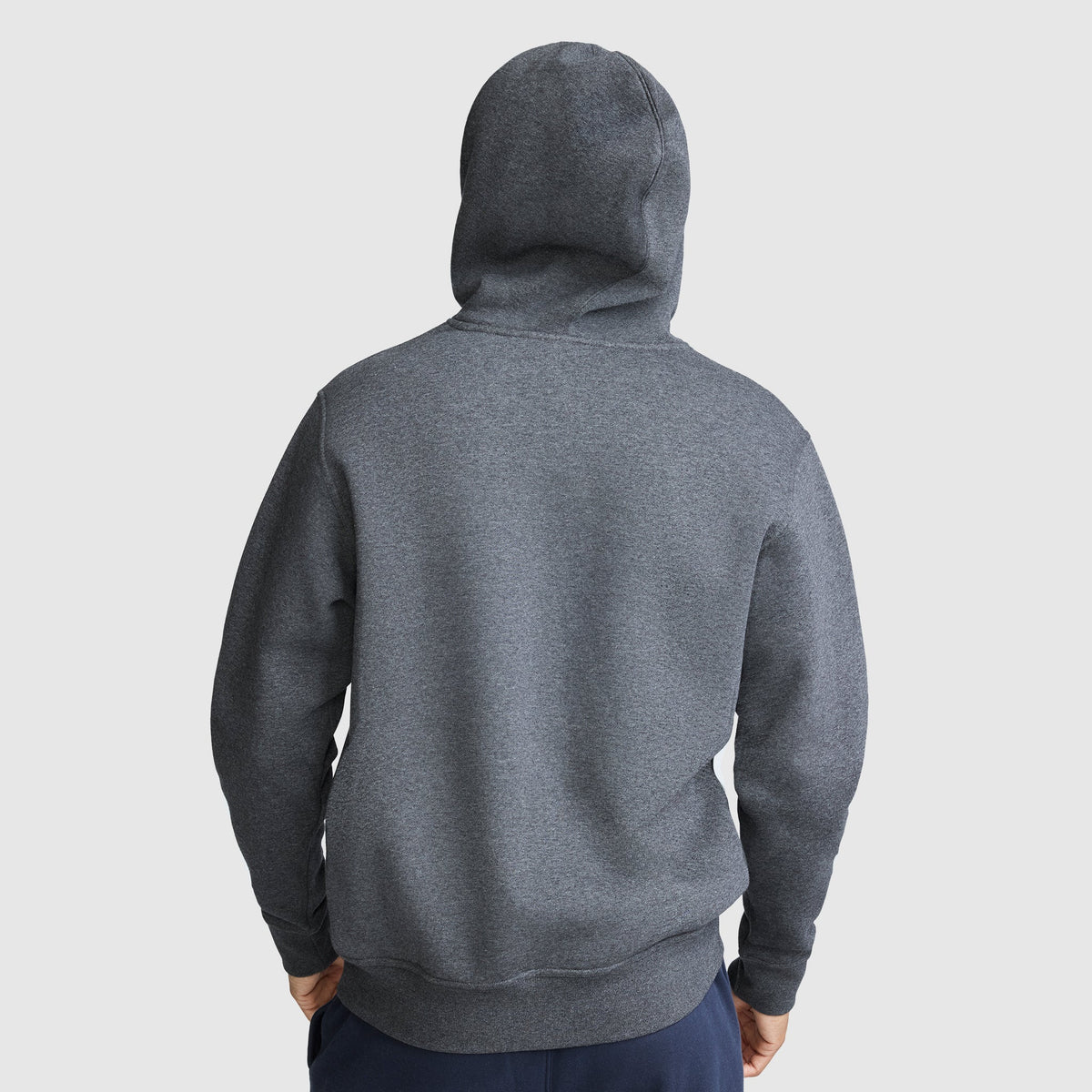 A person is seen from the back wearing a Champion Powerblend Full-Zip Hoodie, C Logo, in plain dark gray with the hood up and hands resting in front. They are also dressed in Champion men’s fleece sweatpants with a Powerblend cinched bottom, which adds a sporty touch against the light gray background.