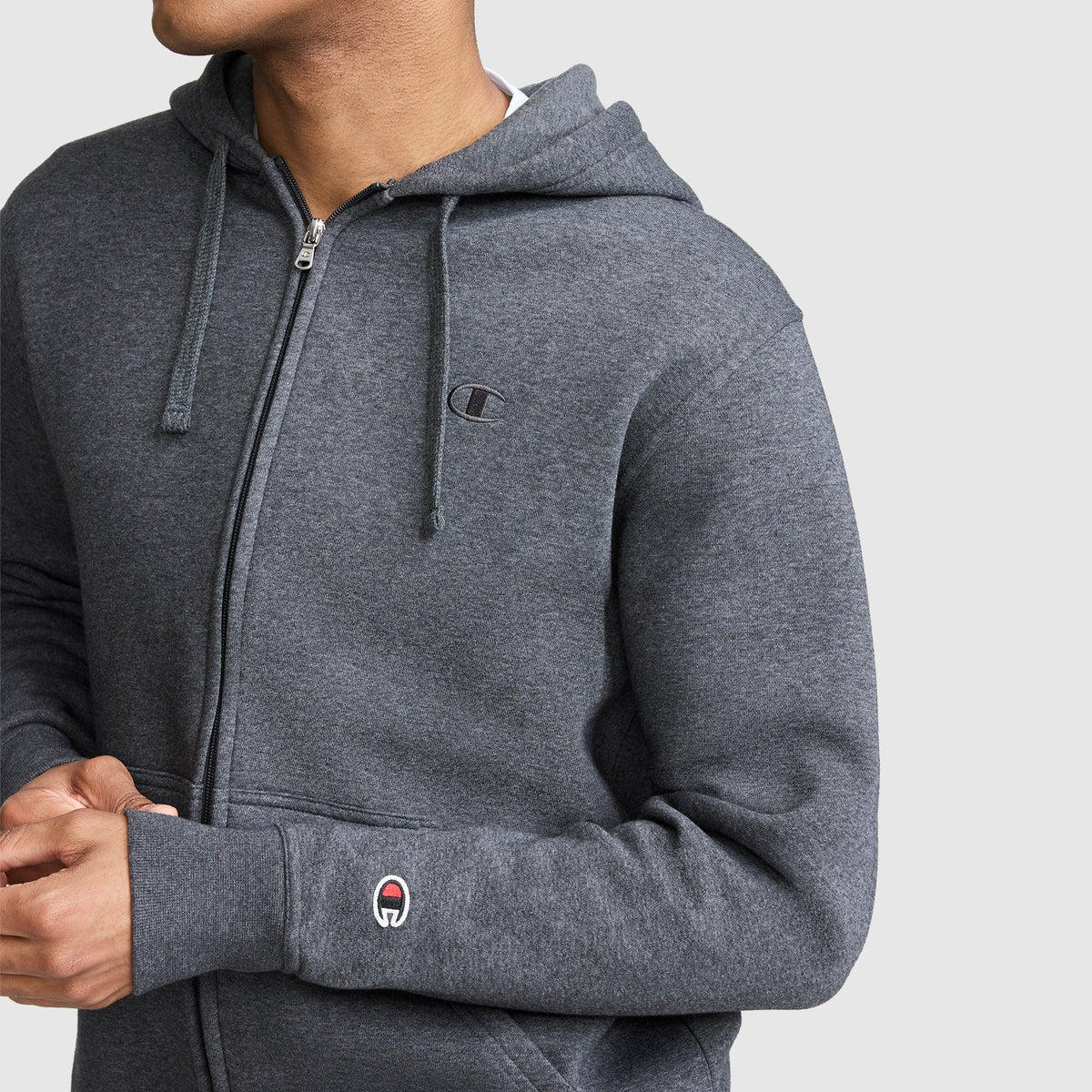 A person wearing the Champion Powerblend Full-Zip Hoodie, C Logo in gray stands against a plain light gray background, paired with Champion men's sweatpants crafted from soft brushed fleece.