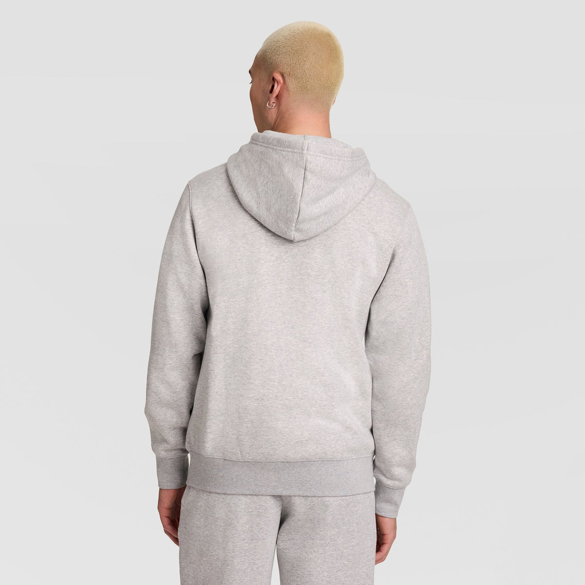 A person with short blond hair is seen from behind, wearing a Champion Powerblend Full-Zip Hoodie with C Logo and matching light gray sweatpants, standing against a plain light background.
