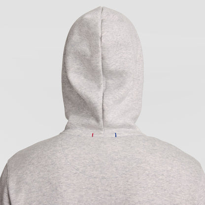A person wearing a light gray Champion Powerblend Full-Zip Hoodie, C Logo, with the hood up is shown from behind against a plain light background. Two small stitches, one red and one blue, are visible on the back of the men’s sweatshirt.