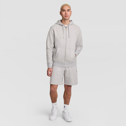 A person stands facing forward, wearing a light gray Champion Powerblend Full-Zip Hoodie, C Logo, paired with matching shorts, white socks, and white sneakers against a plain white background.
