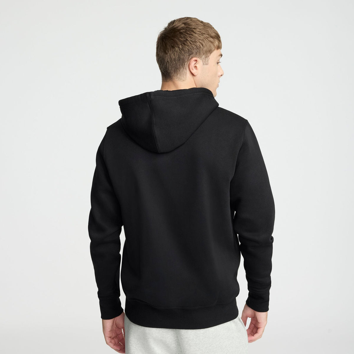 A person wearing a Champion Powerblend Full-Zip Hoodie, C Logo in black and light gray pants stands facing away from the camera against a plain white background.