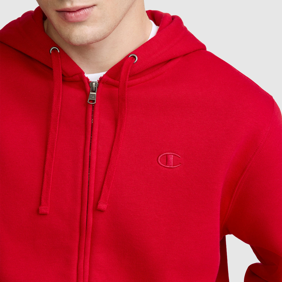 A person is shown from the shoulders up against a plain background, wearing the Champion Powerblend Full-Zip Hoodie, C Logo in bright red with a small embroidered logo on the left chest, paired with Champion Men's Powerblend Sweatpants featuring a cinched bottom.