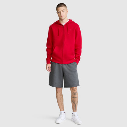 A person wearing the Champion Powerblend Full-Zip Hoodie with a C logo in red, paired with gray men's fleece sweatpants featuring a cinched bottom and white sneakers, stands facing forward. The individual has short hair and visible leg tattoos. The background is plain and light gray.