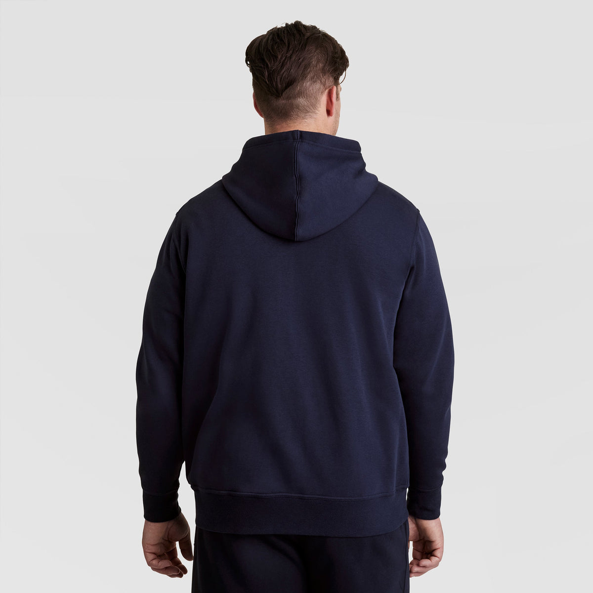 A person wearing a dark blue Champion Powerblend Full-Zip Hoodie, C Logo - Big & Tall stands facing away from the camera against a light gray background.