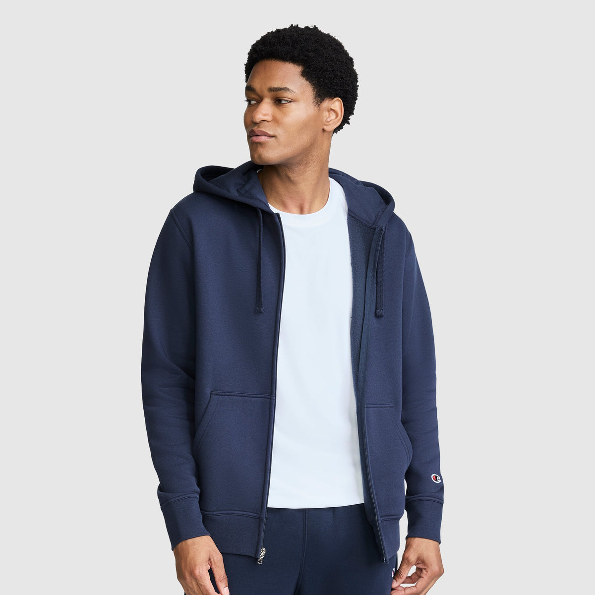 A person wearing a navy blue Champion Powerblend Full-Zip Hoodie, C Logo, with a small logo on the left cuff.