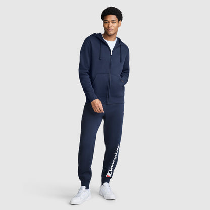 A person wearing a navy blue Powerblend Full-Zip Hoodie, C Logo, matching sweatpants, and white sneakers.