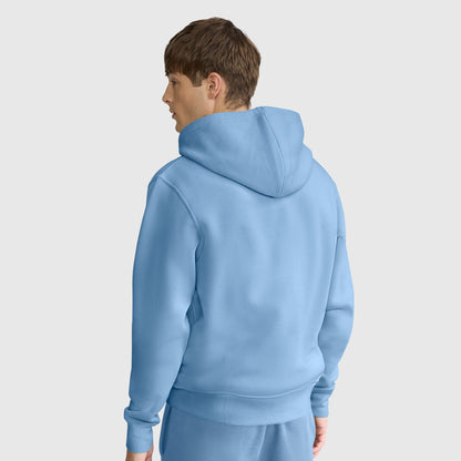 A person with short brown hair is wearing a light blue Champion Powerblend Full-Zip Hoodie, C Logo, paired with matching pants. They are standing and facing away, looking to the left, against a plain light background.