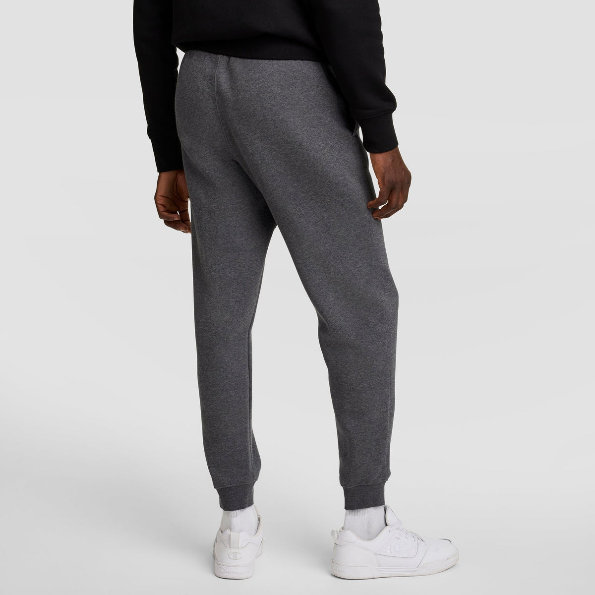 A person is shown from the back wearing Champion Powerblend Joggers, C Logo in dark gray, paired with a black sweatshirt and white sneakers against a plain light gray background.