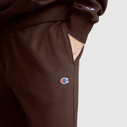 A person wearing Champion’s Powerblend Joggers, C Logo, paired with a matching sweatshirt, rests their hand in the pocket. Both garments feature the Champion logo and are shown against a plain light gray background.