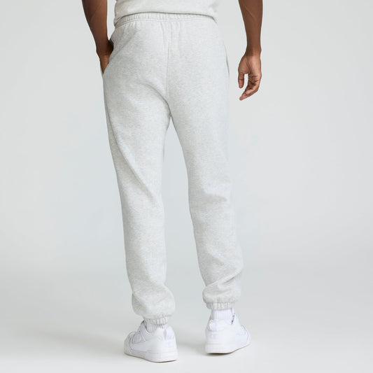 A person stands with their back to the camera, wearing light gray Champion Powerblend Sweatpants, Cinched Hem, C Logo - Big & Tall, featuring an elastic waistband and cuffs, hands in pockets for a relaxed look.