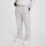 A person wears Champion Powerblend Sweatpants, Open Hem, C Logo - Big & Tall in light gray with a matching sweatshirt and white sneakers, standing hands-in-pockets against a plain white background.