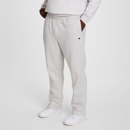 A person wears Champion Powerblend Sweatpants, Open Hem, C Logo - Big & Tall in light gray with a matching sweatshirt and white sneakers, standing hands-in-pockets against a plain white background.